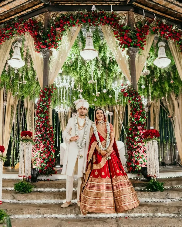 A breathtaking moment for our couple, standing before a mandap rich with red roses and traditional elements. We design wedding stages that are not just backdrops, but the heart of your ceremony, creating a grand and sacred space for your vows.