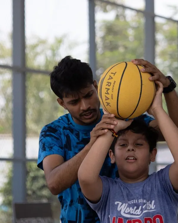 The foundation of a great player is great technique. Here, we are providing hands-on guidance to correct a young player's shooting form, ensuring he builds the right muscle memory from day one. This personal attention is key to our beginner basketball training.