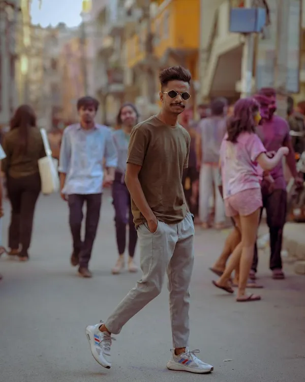 Capturing the vibe of the city streets, this portrait has a cool, candid feel. The blurred background with people celebrating Holi adds energy and context, making it a dynamic lifestyle shot.