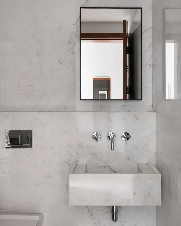 This bathroom in the Collectors House is a study in minimalism, crafted from a single type of marble. The custom-carved sink appears to grow out of the wall, creating a seamless and sculptural look.