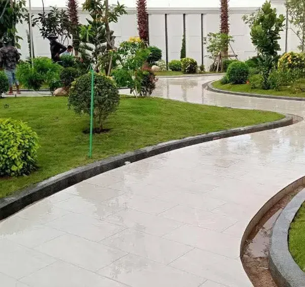 A newly installed landscape for a commercial property, featuring curving paved pathways, fresh turf, and a variety of shrubs and trees. A worker is seen giving the final touches, showcasing our hands-on approach.