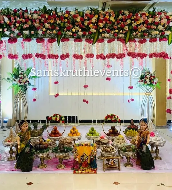 An elegant and modern Seemantha setup with a white and pink floral theme. The hanging flower strings and clean arrangement of offering plates create a sophisticated and dreamy atmosphere for the baby shower.