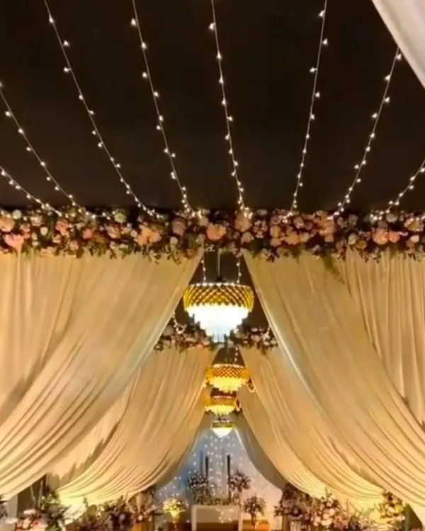 This is an example of an elegant entranceway I can create, using soft fabric drapes, floral arrangements, and a ceiling of fairy lights for a magical effect.