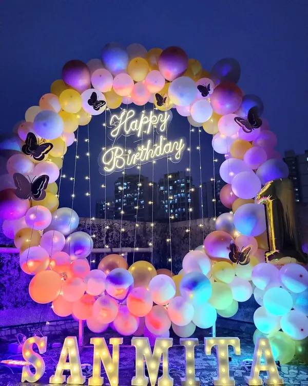 A stunning butterfly-themed birthday decoration set up on a terrace. The balloon ring with a neon sign looks beautiful against the night sky.