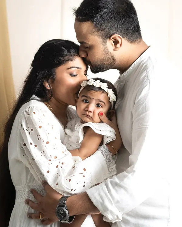 A beautiful family embrace, with parents showering their little one with love. This is a classic family portrait that shows the warmth and protection that surrounds a child.