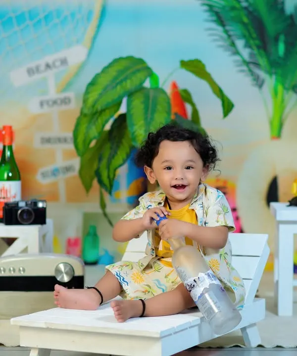A happy baby enjoying our beach theme, complete with a miniature beach chair, surfboards, and even tiny bottles of Coca-Cola for a vintage vibe.