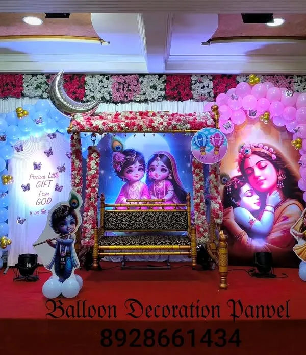 A grand stage decoration for a 'Dohale Jevan' or baby shower in a hall. The setup features a beautiful cradle, traditional backdrops, and balloon arches in pink and blue.