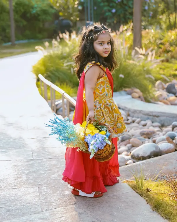 A little princess in a beautiful garden, holding a basket of flowers. The soft, natural light and serene path create a fairytale-like setting for this outdoor portrait.