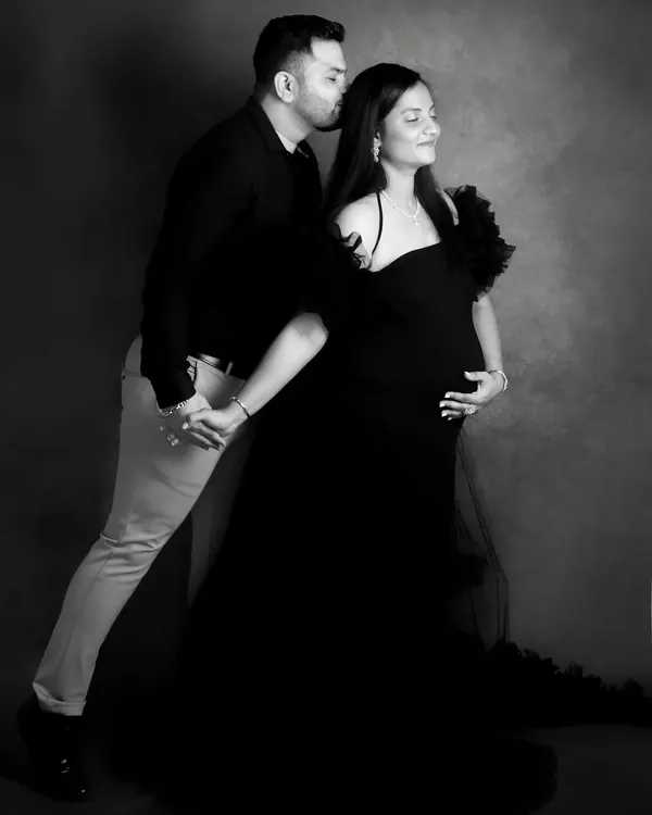 A full-length black and white portrait that feels like a classic dance pose. The contrast and lighting beautifully highlight the couple's connection and the elegant lines of the maternity gown.