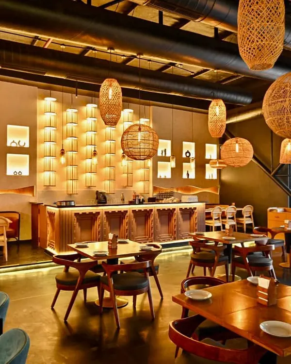 We craft immersive dining environments that captivate guests from the moment they arrive. This wide view of the Indus Flavour restaurant highlights our approach to atmospheric design, where layered lighting with wicker pendants, a variety of seating arrangements, and a warm, earthy palette combine to create an unforgettable fine dining experience.