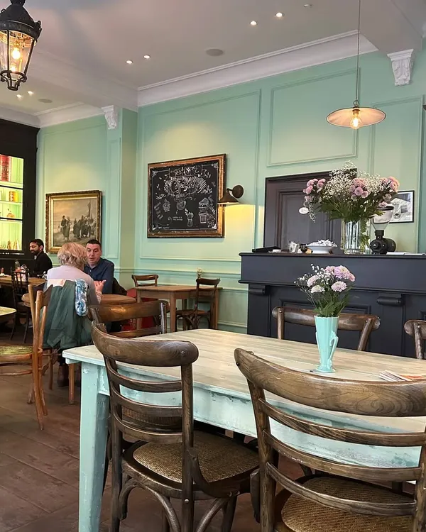 The serene atmosphere of a European café, with its soft mint-green walls, classic wooden furniture, and curated artwork. These spaces are a masterclass in creating an inviting ambiance that encourages people to linger.