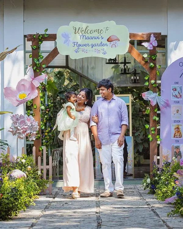 A family portrait at a beautiful fairy-garden-themed first birthday party. The personalized entrance and milestone board add a lovely, sentimental touch to the celebration.