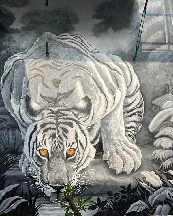 The full view of the 'Pili Kula' tiger mural, showing the powerful animal as it crouches to drink from a stream. The monochromatic color scheme with piercing orange eyes creates a dramatic effect in this clubhouse atrium.