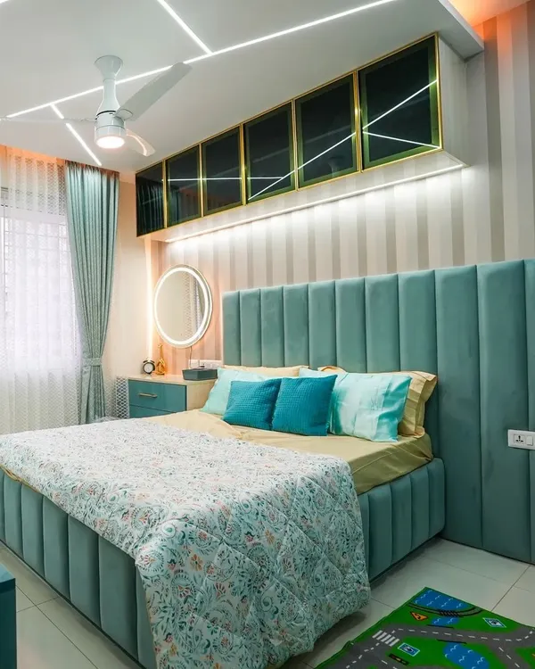 The final look of a beautiful kid's bedroom. The channel-tufted upholstered bed in teal is the star, complemented by striped wallpaper, overhead cabinets with gold trim, and playful geometric ceiling lights.