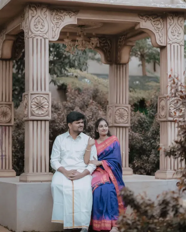 A serene pre-wedding portrait of a couple in traditional South Indian attire. The ornate stone gazebo provides a beautiful, classic backdrop that complements their outfits perfectly.