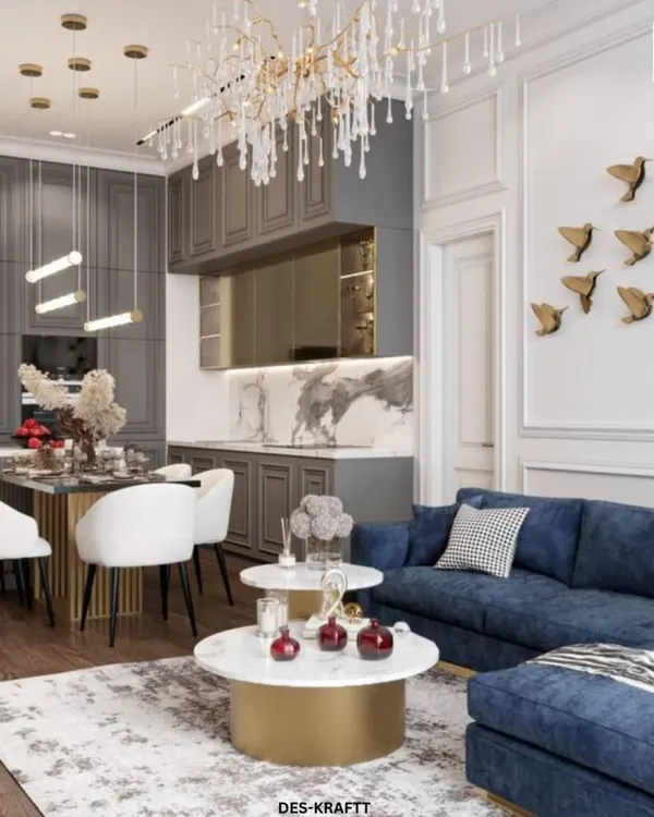 A complete view of this open-concept living space, showing how the plush blue sofa, marble tables, and elegant dining area coexist harmoniously under a stunning crystal chandelier.