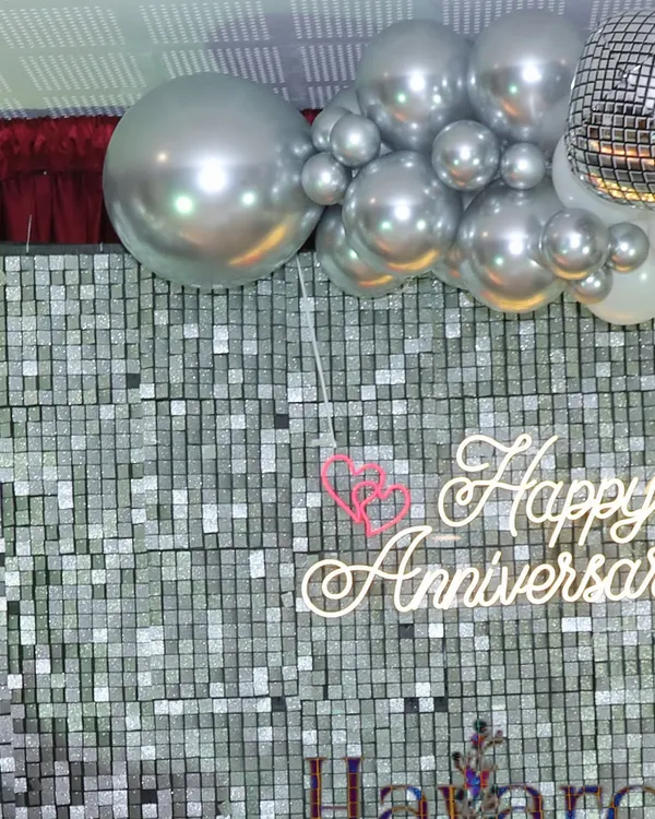 A close-up of a 'Happy Anniversary' neon sign against a silver sequin backdrop. It's a perfect, shimmery detail for a special celebration.