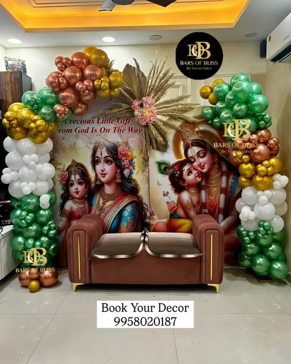 A divine Radha Krishna themed backdrop for a traditional baby shower. The beautiful printed backdrop is framed by an arch of green, white, and gold balloons, creating a blessed and serene atmosphere.