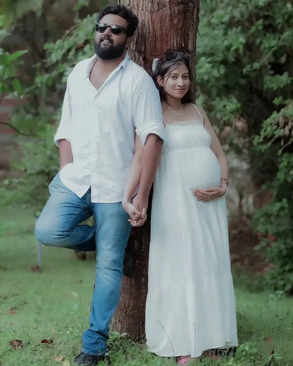 A relaxed and stylish portrait of the expecting couple. The natural park setting and their coordinated white outfits create a fresh and timeless look for their maternity shoot.