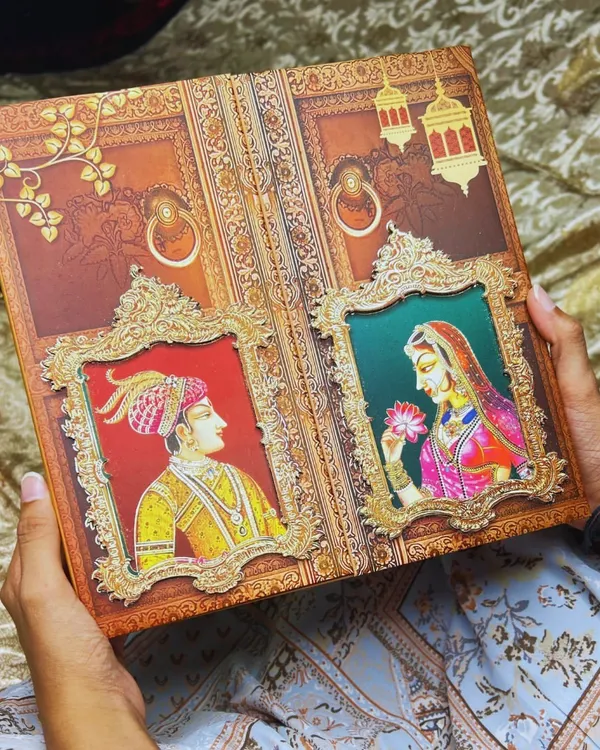 A closer look at the handcrafted Raja-Rani invitation, held to show its substantial feel and detailed artistry. This design is not just an invite, but a 'pavitra bandhan ki pehli anmol nishani' (the first precious symbol of a sacred bond).