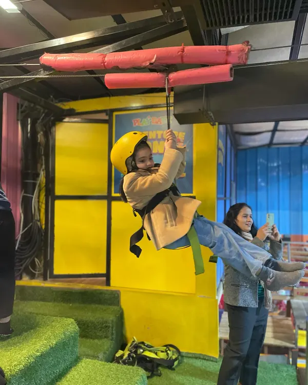 Our indoor zip-line is a huge hit with adventurous kids. Here, a young guest gets ready to fly across the play area, fully secured in a safety harness and helmet.