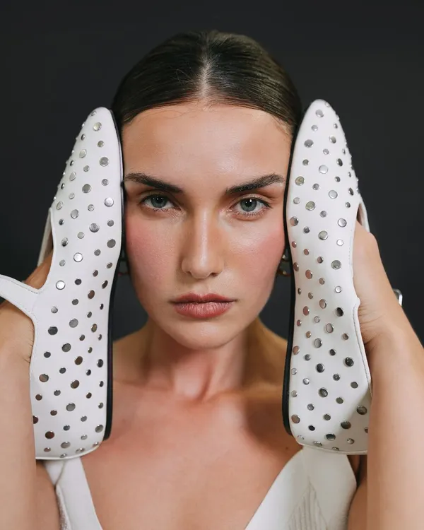 A creative and unconventional beauty shot for a model's portfolio, using a pair of white studded shoes to frame the face.