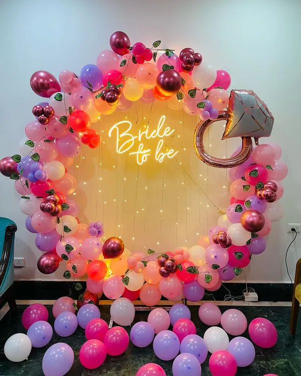 Our signature "Bride to be" ring backdrop is the perfect centerpiece for any bridal shower. This setup features a lush garland of pink, purple, and burgundy balloons, a sparkling diamond ring foil balloon, and a warm neon sign, all framed by delicate fairy lights for that magical glow.