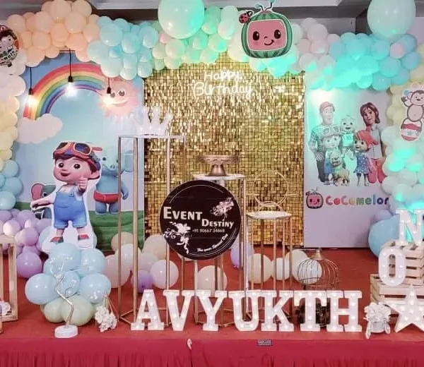 A fantastic Cocomelon theme for a first birthday party. This setup includes a gold sequin backdrop, a pastel balloon arch, and cutouts of all the favorite Cocomelon characters.
