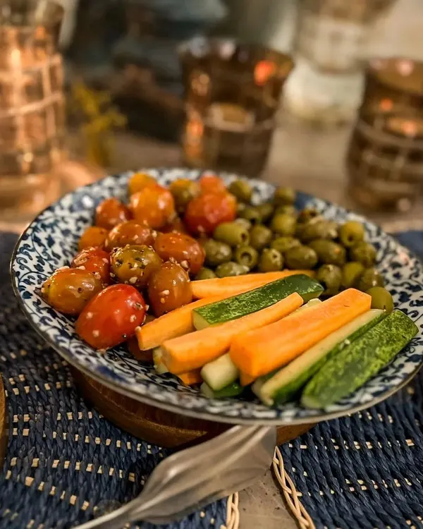 A bowl of fresh vegetables and olives, part of a festive setup for a Diwali dinner. The candlelit ambiance adds a warm and inviting glow to the dining experience.