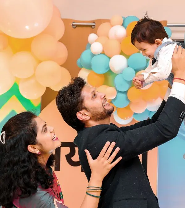 A beautiful family portrait capturing a moment of pure joy. The father lifts his son, and the mother looks on with a smile, all against the backdrop of their custom-designed first birthday party.