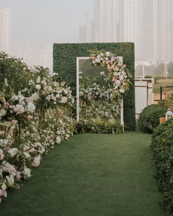A chic, serene, and earthy entrance for a garden reception. Guests walked through a pathway lined with flowers to a mirrored doorway set in a hedge wall, creating a magical "secret garden" effect.