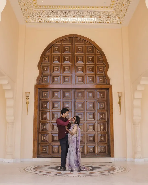 A beautiful couple portrait in front of a grand wooden door at Anantara, Jaipur. The royal architecture of Rajasthan provides an unparalleled backdrop for wedding photography.