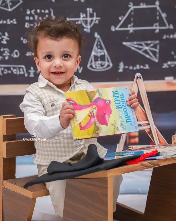 Ready to learn with a smile. This little scholar is excited for his classroom-themed photoshoot, holding up his favorite dinosaur book.