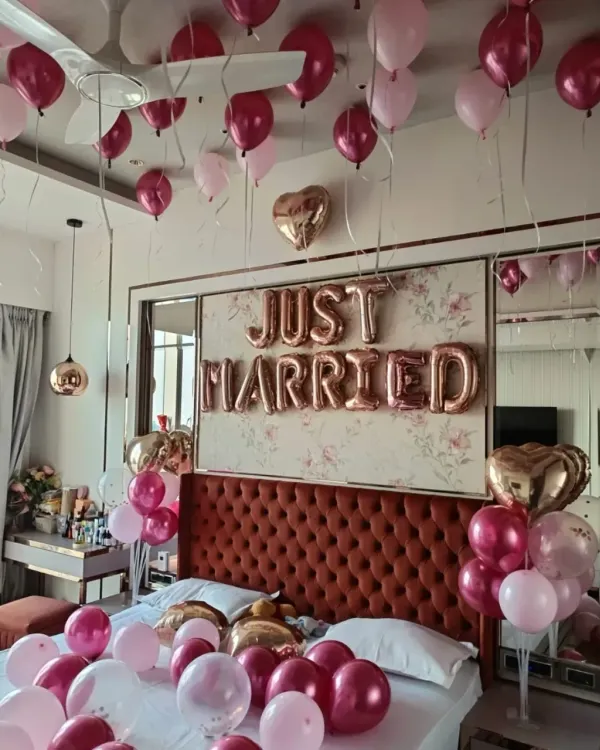 A classic "Just Married" bedroom decoration. The room is filled with pink and white balloons, with rose gold foil letters on the wall to celebrate the newlyweds.
