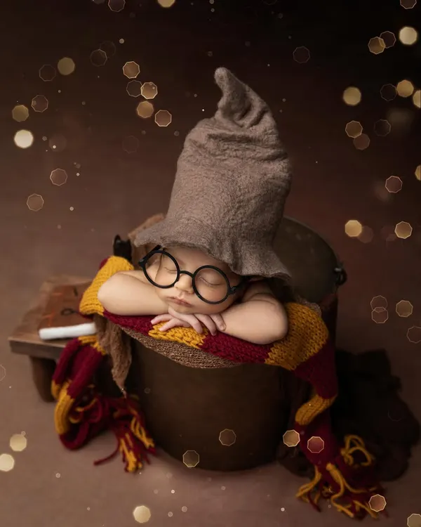 A little wizard in the making. This Harry Potter themed newborn shoot features the iconic sorting hat, glasses, and a Gryffindor scarf, complete with a magical bokeh background.