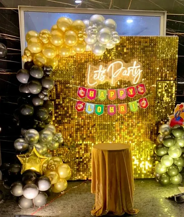 A festive Lohri celebration setup. The decor features a gold shimmer wall, a "Happy Lohri" banner, and a black and gold balloon arrangement.