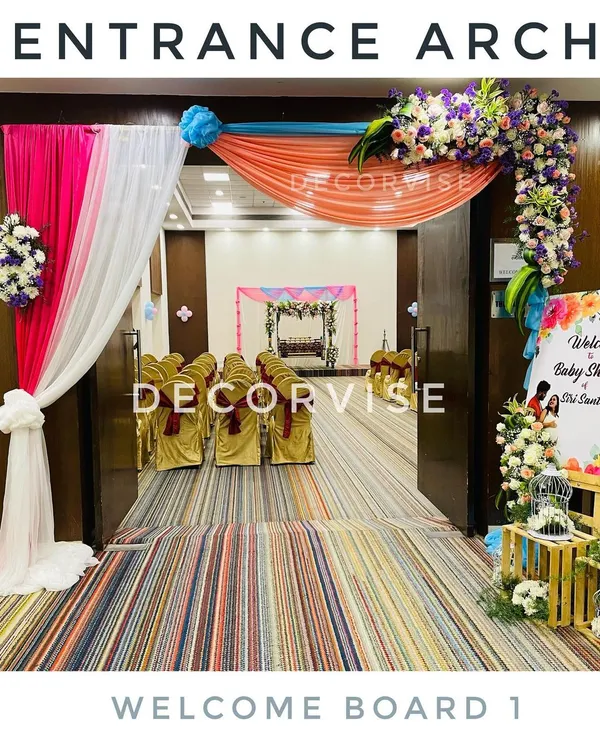 A welcoming entrance we created for a baby shower, featuring colourful drapes in pink, white, and orange, accented with fresh floral arrangements. This arch provides a beautiful first impression and a glimpse of the main decor inside.