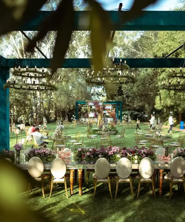 A beautiful long shot of the lakeside reception setup. The open-sided structure, adorned with greenery chandeliers, allowed guests to dine while enjoying the stunning natural surroundings.
