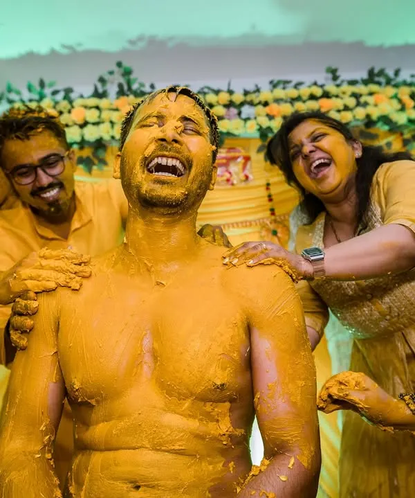 The very definition of a joyful Haldi. The groom is laughing uncontrollably as his friends and family playfully smear him with turmeric paste.