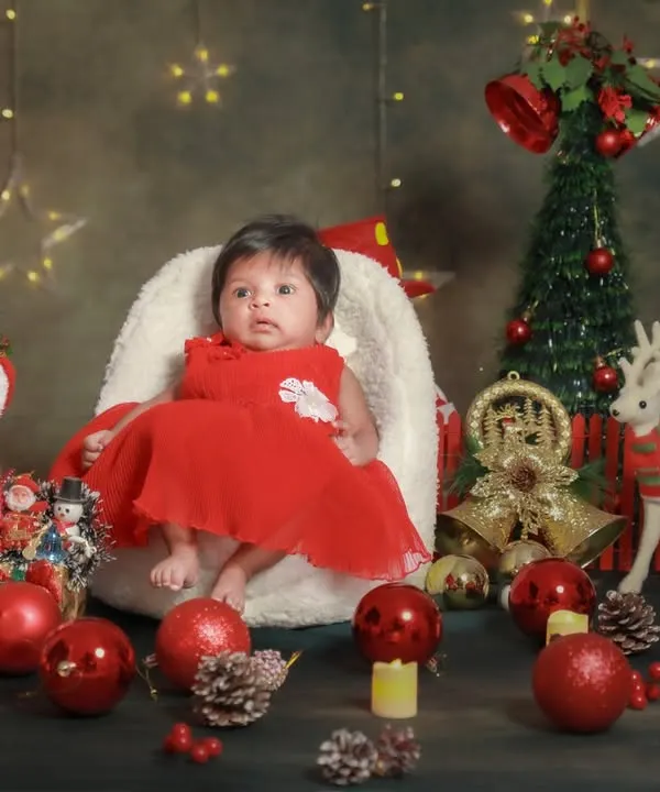 Baby's first Christmas! This little one is sitting so sweetly in her festive red dress, surrounded by all the magic of the season.