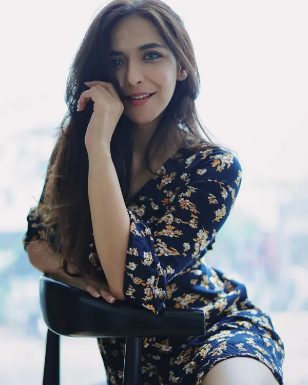 A relaxed portrait of a woman in a floral dress, seated by a window. Her warm smile and direct eye contact create an inviting and confident image, showcasing how natural light can be used to create beautiful, soft-lit fashion shots.