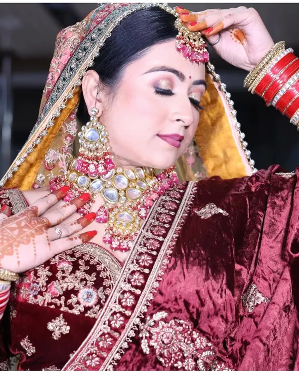 A classic bridal look in rich maroon velvet. This lehenga features intricate embroidery and is paired with a stunning Kundan and pearl jewellery set, perfect for making a timeless statement on your wedding day.