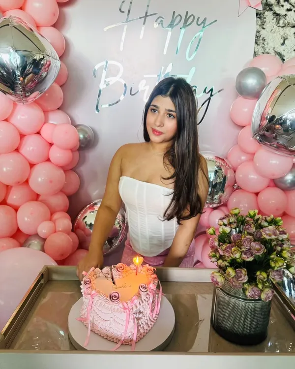 A perfect birthday moment. The birthday girl with her cake, set against the pink and silver backdrop we designed. The setup includes a custom 'Happy Birthday' sign and fresh flowers to complete the celebratory feel.