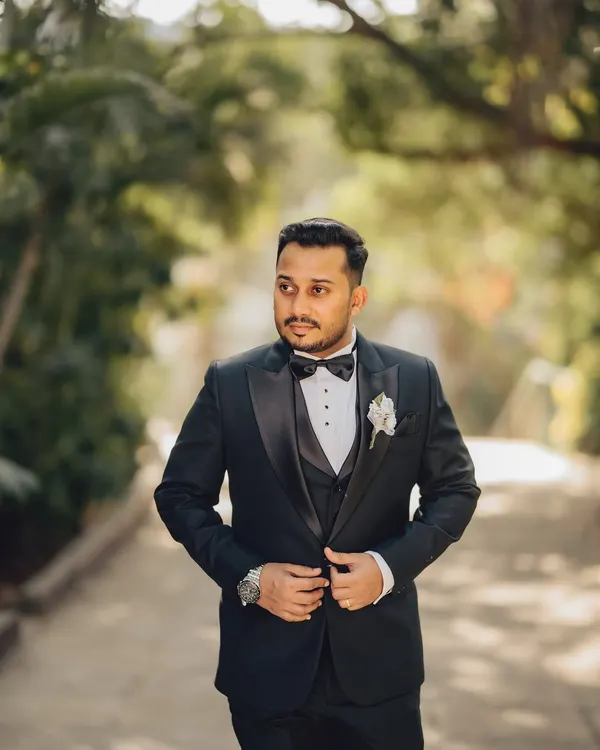 A classic portrait of the groom in his tuxedo. This shot captures his sharp attire and a confident look, set against a natural outdoor backdrop.