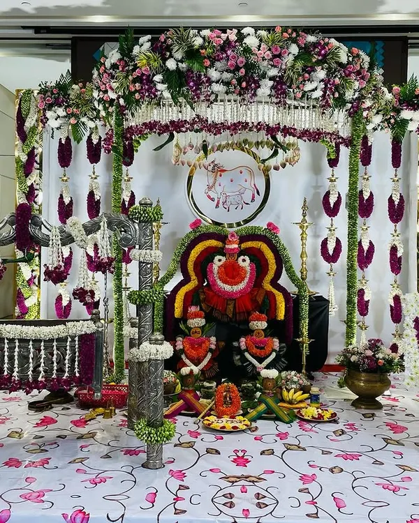 This is a complete view of a traditional naming ceremony setup for baby Vihaa. It includes a silver-plated cradle and a backdrop with deity arrangements, all adorned with fresh flower garlands and traditional elements.