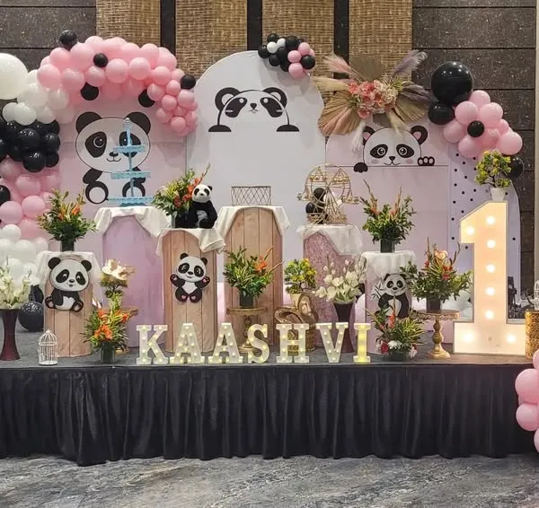 This popular Panda theme is perfect for a first birthday. The setup features a custom backdrop with cute panda illustrations, pink and black balloons, and a light-up number '1'.