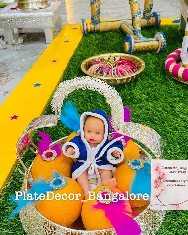 A baby boy themed platter for a seemantham ceremony. The basket contains decorated oranges and a cute baby doll dressed in a blue robe, accented with blue and pink feathers.