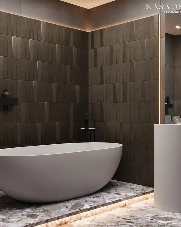 This bathroom achieves a moody, tranquil atmosphere through a masterful play of textures. The back wall features bold, vertically-oriented 3D tiles that create a sense of height, while the terrazzo-style flooring adds a layer of visual complexity. The freestanding tub becomes the centerpiece in this minimalist yet luxurious retreat.