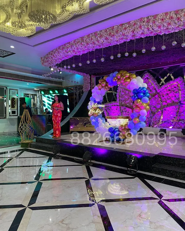 This photo shows the scale of a grand 'Welcome Baby' stage I designed for a banquet hall. The circular balloon arch and neon sign create an impressive centerpiece for the event.