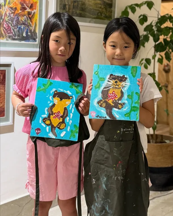 Two young artists proudly holding up their adorable otter paintings. It's wonderful to see them bring their ideas to life with acrylics on canvas during our guided sessions.